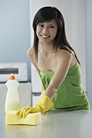woman in kitchen cleaning counter with sponge, smiling at camera - Asia Images Group