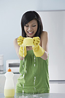 woman cleaning kitchen, squeezing water from sponge onto counter, smiling - Asia Images Group