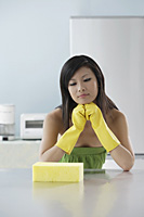 woman in kitchen, looking at sponge, thinking, cleaning - Asia Images Group