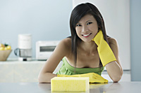 woman in kitchen with sponge, wearing gloves, looking at camera, smiling - Asia Images Group
