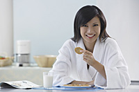 woman in kitchen wearing bathrobe, holding cooking, smiling at camera, reading magazine - Asia Images Group