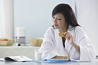 woman in kitchen wearing bathrobe, holding cooking, reading magazine - Asia Images Group