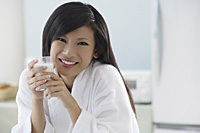 woman in kitchen, holding glass of milk, smiling at camera - Asia Images Group