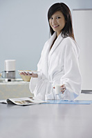 woman in kitchen, holding glass of milk and plate of cookies, smiling at camera - Asia Images Group