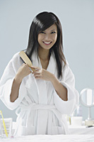 woman wearing bathrobe, brushing hair and smiling at camera - Asia Images Group