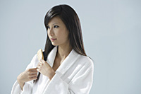 woman wearing bathrobe, brushing hair and looking away from camera - Asia Images Group