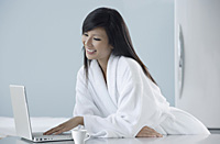 woman wearing bathrobe in kitchen, looking at computer, laptop, smiling - Asia Images Group