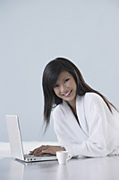 woman wearing bathrobe, smiling and working on laptop computer, smiling at camera - Asia Images Group
