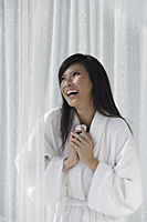 woman in bathrobe, holding phone to chest and laughing - Asia Images Group