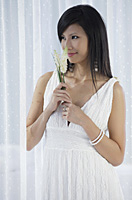 woman in white dress holding flowers and smelling flowers - Asia Images Group