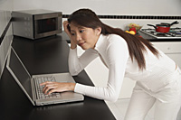 Woman leaning on counter, looking at laptop / computer. - Asia Images Group