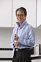 Man in kitchen, buttoning his shirt and tie loose around neck.  smiling at camera.  Getting ready for work. - Asia Images Group