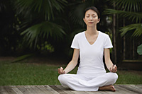 Woman in tropical setting, meditating on porch, eyes closed, in yoga OM posture. - Asia Images Group