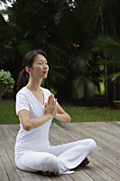 Woman sitting on porch, in tropical setting.  legs crossed, hands in namaste, yoga posture. eyes closed - Asia Images Group