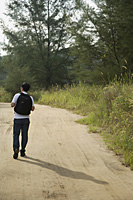 Man walking down dirt road, hiking, back to camera - Asia Images Group