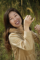 Woman outside standing in tall grass, smiling at camera - Asia Images Group
