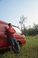 Man leaning against red van, outdoors in nature - Asia Images Group