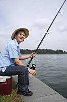 Man sitting on cooler, fishing with fishing pole - Asia Images Group