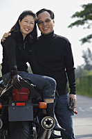 Mature couple looking at camera, woman sitting on motorcycle - Asia Images Group