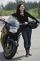 Woman leaning against motorcycle, holding helmet, looking away from camera - Asia Images Group