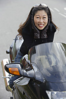 Woman sitting on motorcycle, hands to face, smiling at camera - Asia Images Group