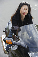 Mature woman sitting on motorcycle, smiling at camera - Asia Images Group