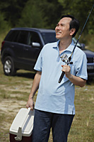 Mature man holding fishing pole and cooler, smiling - Asia Images Group