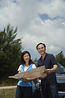 Woman and man standing by car, reading map, looking at camera - Asia Images Group