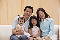 portrait of Family of 4, mom, dad and two daughters, sitting on couch, smiling, looking at camera - Asia Images Group