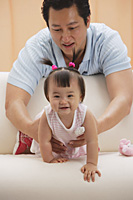 father and baby girl, father holding girl as she crawls on couch - Asia Images Group