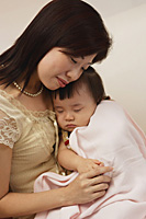 Mother holding baby girl in arms, baby girl wrapped up in blanket, peaceful - Asia Images Group