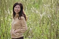 woman standing in tall grass, nature, smiling at camera - Asia Images Group