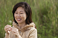 woman holding flower, standing in tall grass, outdoors - Asia Images Group