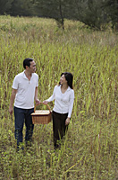 Man and woman walking through nature carrying picnic basket - Asia Images Group