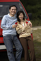 Man and woman leaning against red van, smiling at camera, camping - Asia Images Group
