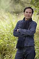 Man wearing scarf, standing outdoors in nature, smiling at camera - Asia Images Group