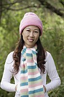 Woman wearing hat and scarf outdoors in nature, smiling at camera - Asia Images Group