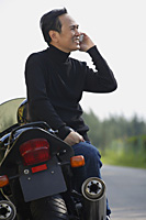 Mature man leaning on motorcycle, talking on mobile phone - Asia Images Group