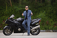 Man sitting on motorcycle, giving thumbs up - Asia Images Group