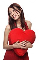 Young woman holding red heart shaped pillow, looking away - Asia Images Group
