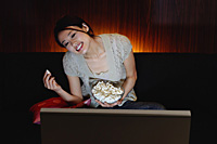 Young woman eating popcorn and watching TV - Asia Images Group