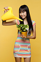 Young woman watering plant with bright yellow watering can - Asia Images Group