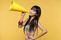 Young woman holding yellow megaphone and smiling at camera - Asia Images Group