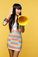 Young woman talking through yellow megaphone, hand to ear - Asia Images Group