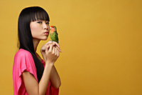 Young woman with lovebird on her hand, kissing bird - Asia Images Group