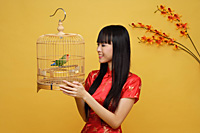 Young woman holding lovebird in bird cage - Asia Images Group