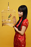 Young woman holding lovebird in bird cage, looking at bird - Asia Images Group