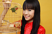 Young woman holding lovebird in bird cage, smiling - Asia Images Group