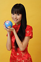 Woman wearing cheongsam and holding globe in hands - Asia Images Group