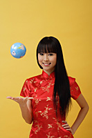 Young woman wearing red cheongsam and throwing globe in the air - Asia Images Group